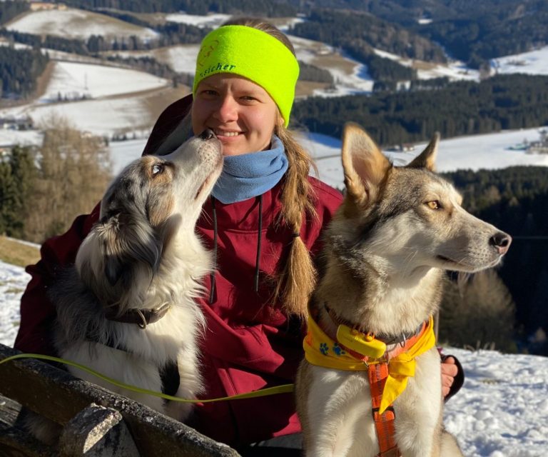 Junge Frau mit floralem Haarband und lächelndem Gesicht vor einer grünen Wand.