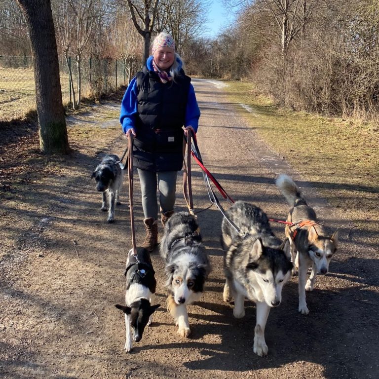 Frau mit langen Haaren und Kopfbedeckung schnuppert an einem Hund.