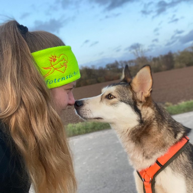 Pfotensicher München Frau mit langen Haaren und Kopfbedeckung schnuppert an einem Hund.